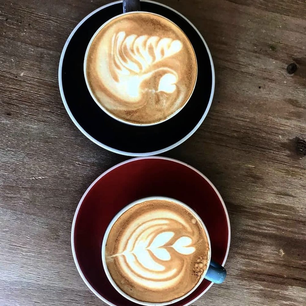 Dos cafés con latte art vistos desde arriba sobre una mesa de madera